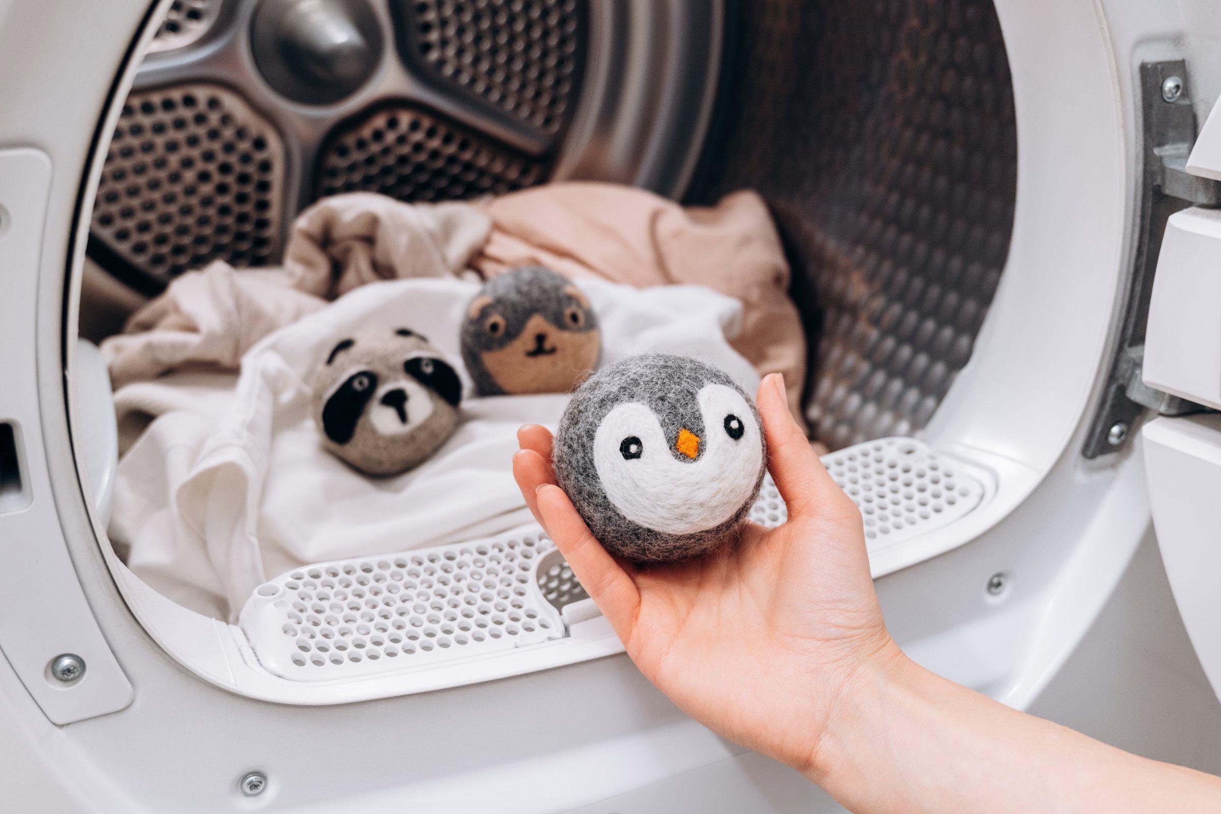 A hand placing a Wooly Heroes dryer ball into a tumble dryer full of laundry