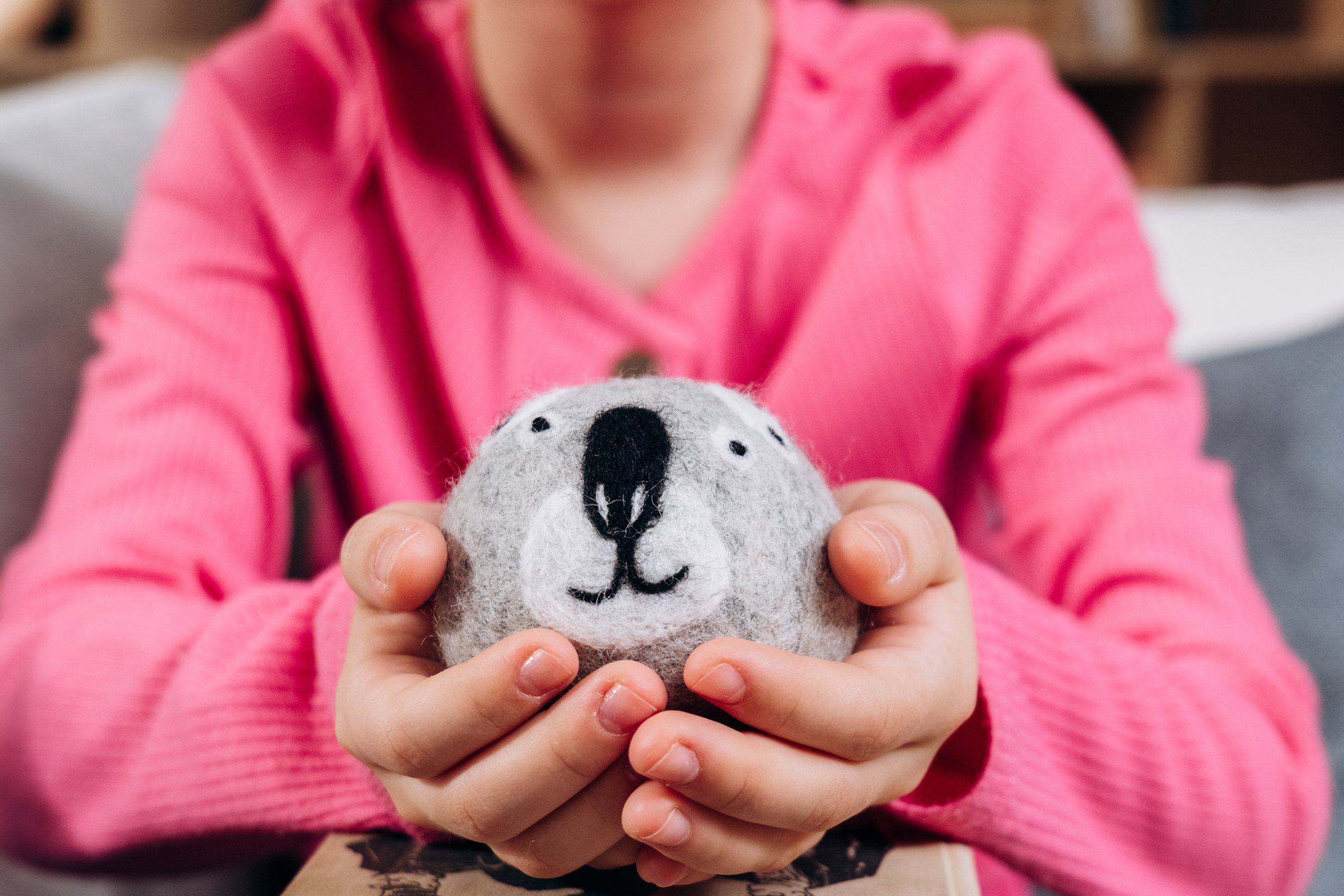 Hands holding a hand-felted koala dryer ball up close, showing the wool texture