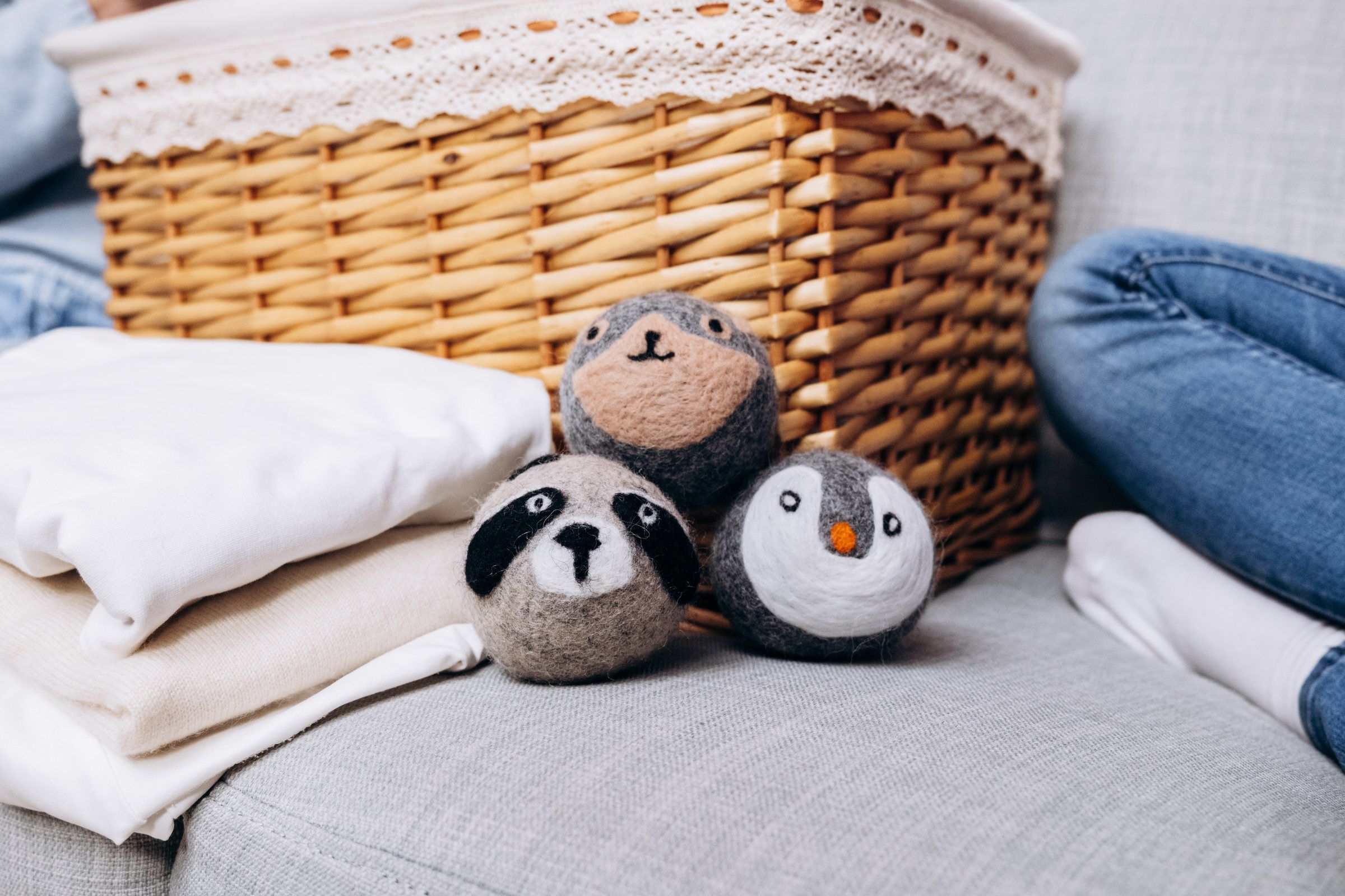 Three animal-faced wool dryer balls on a sofa beside folded laundry